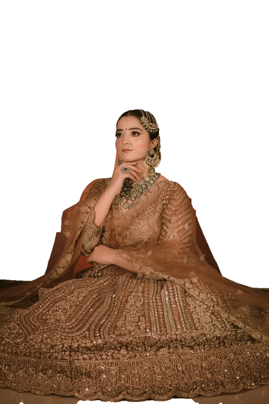 A bride in a gold embroidered lehenga with a sheer dupatta, seated in front of a Mughal arch