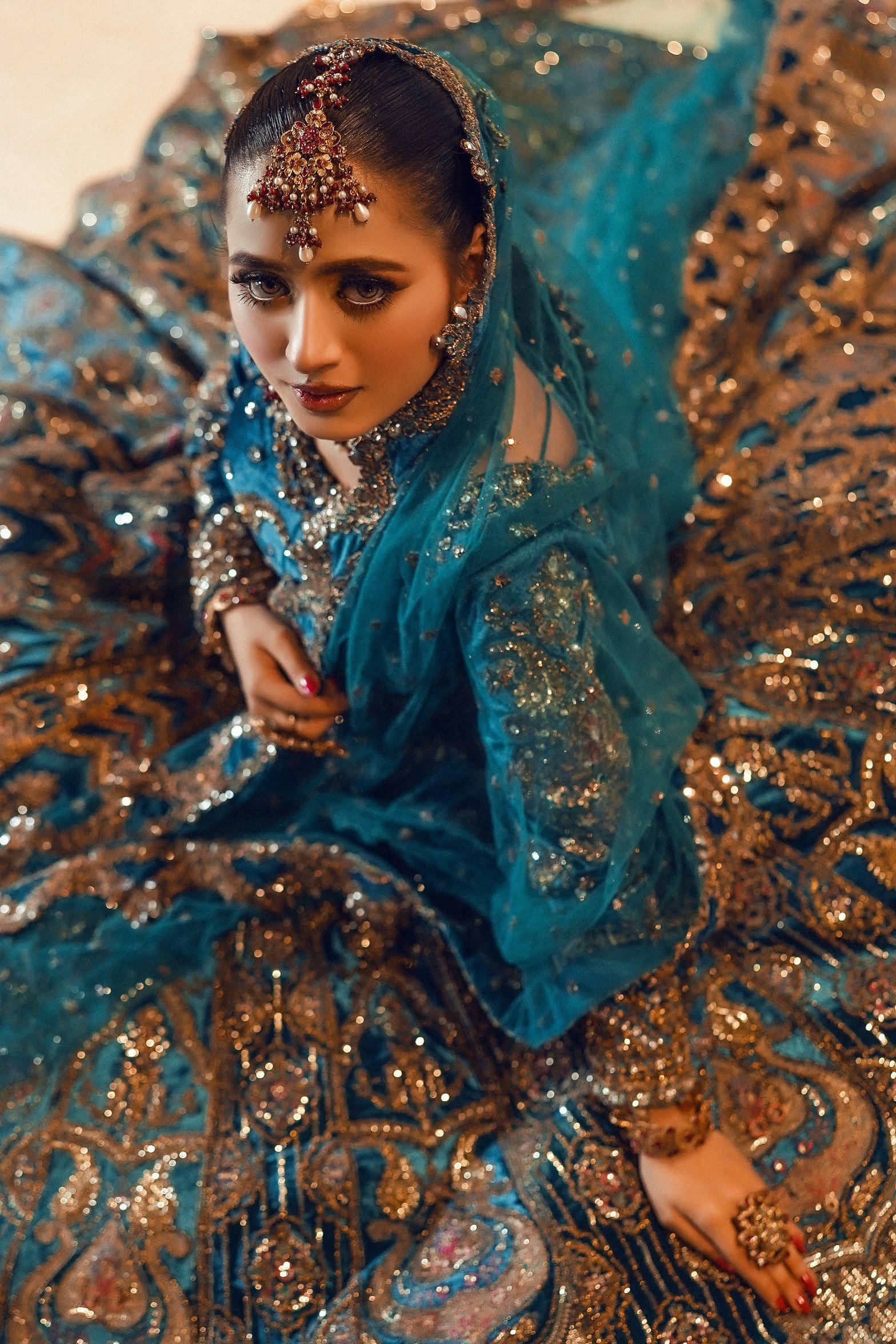 Close-up of a teal velvet bridal outfit covered in hand-sewn gold sequins and zari